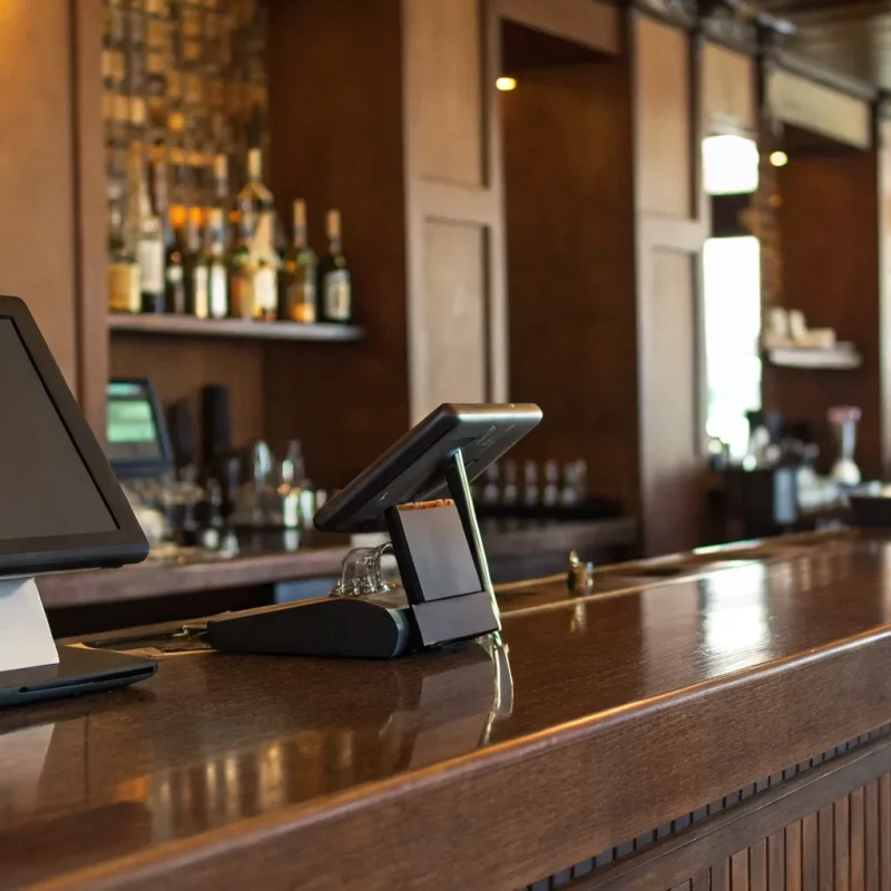 A bar's point of sale system on a wooden counter with liquor bottles on display.